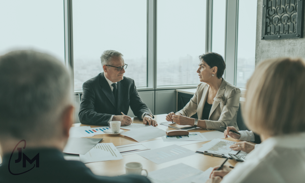 Business leaders in a meeting, pausing to listen and discuss strategy around a table, illustrating self-awareness, trust, and connected leadership.