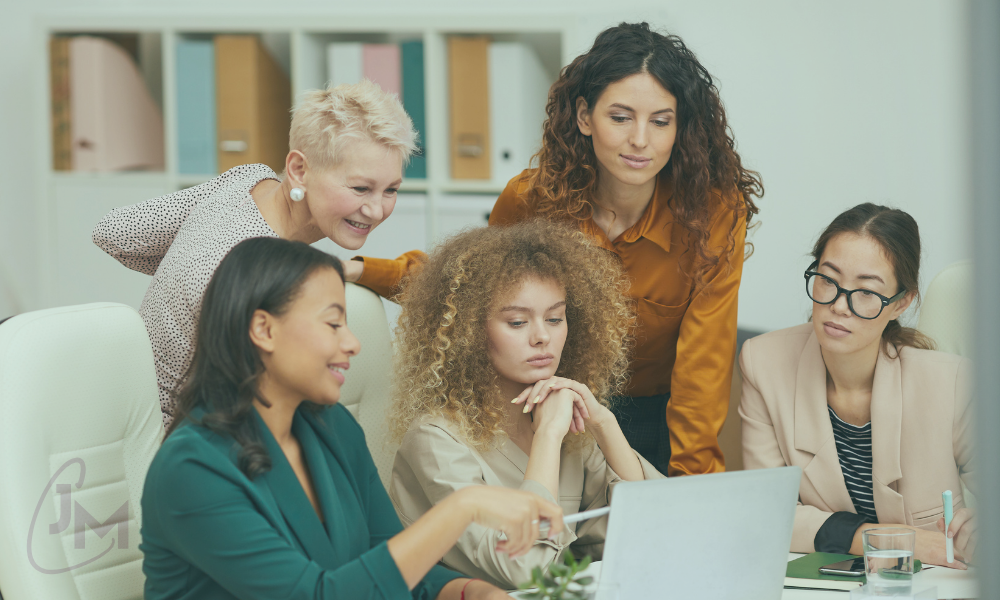 Diverse group of female business leaders collaborating around a laptop in an office meeting