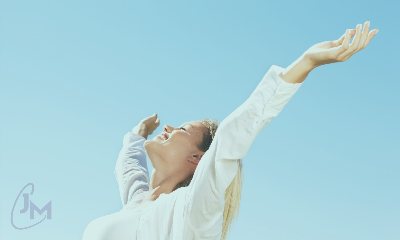 Woman with arms raised toward a clear blue sky, symbolising leadership capacity and the freedom of letting go